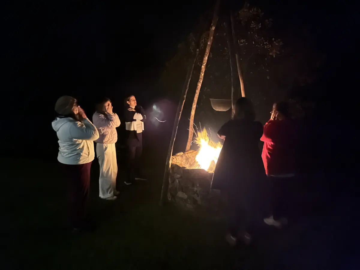 Roda de mulheres reunida em volta do fogo, à noite